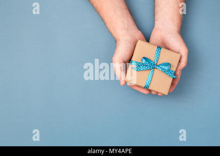 Des Menschen Hände halten Kraftpapier Geschenkbox mit Schleife gebunden. Ansicht von oben, urlaub Konzept. Stockfoto