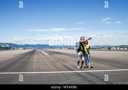 Paar ein selfie bei Gibraltar International Airport, wo eine vierspurige Straße kreuzt die Start- und Landebahn Stockfoto