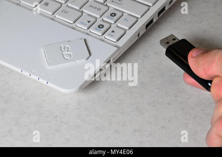 Eine männliche Hand fügt ein Schwarz kompakte USB-Karte in das entsprechende Eingabefeld auf der Seite der weißen Netbook. Der Mensch nutzt moderne Technologien Memo zu speichern Stockfoto