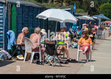 Eine große Familie genießen den Sommer Sonnenschein um einen Tisch mit Sonnenschirm oder im Schatten essen und sprechen an einem warmen Sommertag sitzt, miteinander. Stockfoto