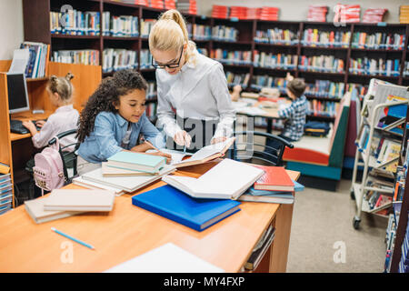 Junge Lehrer helfen Schulmädchen mit Hausaufgaben in der Bibliothek Stockfoto