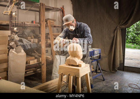Nahaufnahme, junger Mann, Tischler in einem Anzug, Schutzbrille sägen Kopf eines Mannes mit einem Baum, mit einem Winkelschleifer in der Werkstatt, um eine Menge Tools für Stockfoto
