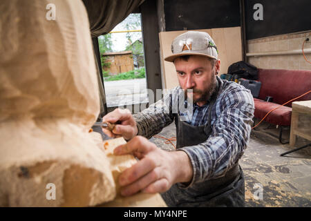 Junger Mann, Tischler in einem Arbeitskleidung sägen Kopf eines Mannes mit einem Baum, mit einem Meißel in der Werkstatt, um eine Menge von Werkzeugen für die Arbeit Stockfoto