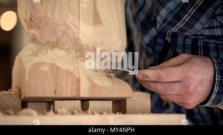 Nahaufnahme, junger Mann, Tischler in einem Arbeitskleidung sägen Kopf eines Mannes mit einem Baum, mit einem Meißel in der Werkstatt, um eine Menge von Werkzeugen für die Arbeit Stockfoto