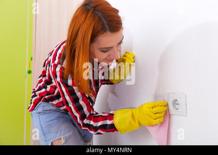 Сlose bis der jungen Frau in Jeans, gelbe Handschuhe und Plaid Shirt ist die Schalter der Wisch-Waschanlage und die Wand mit einem rosa Lappen in das Kinderzimmer mit whit Stockfoto