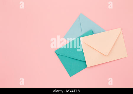 Drei farbige Briefumschläge auf rosa Hintergrund. Minimalistisch gestaltete Komposition, Ansicht von oben, Korrespondenz Konzept. Stockfoto