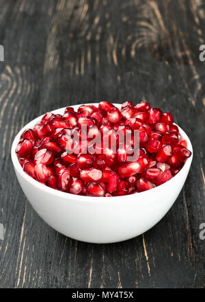 Weiße Schüssel mit Granatapfel Samen auf einer hölzernen Hintergrund schließen gefüllt. Stockfoto