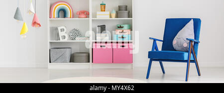 Panorama einer niedlichen Kissen auf einem blauen Sessel und ein Bücherregal mit Boxen und Dekorationen in einem Spaß Kinderzimmer Einrichtung mit weißen Wänden Stockfoto