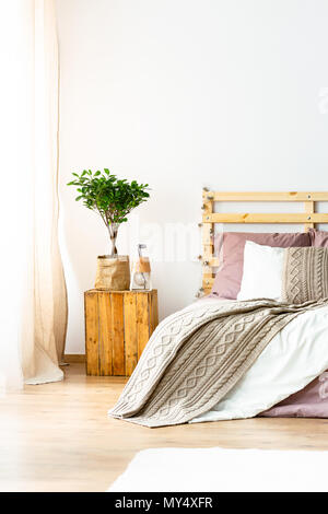 Anlage auf hölzernen Hocker neben dem Bett mit Decke in natürlichen Schlafzimmer Innenraum. Real Photo Stockfoto