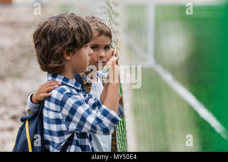 Seitenansicht von niedlichen kleinen Schuljungen über Net auf der Suche nach Fußball-Feld Stockfoto