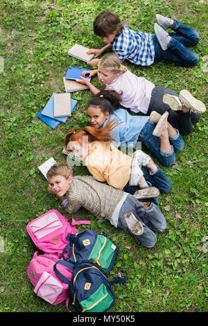 Blick von oben auf die kleine süße Kinder Bücher lesen beim Liegen auf Gras und lächelnd an Kamera Stockfoto