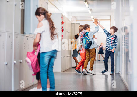 Jungs, fünf in der Schule Flur, während Mädchen, Bücher ins Schließfach Stockfoto