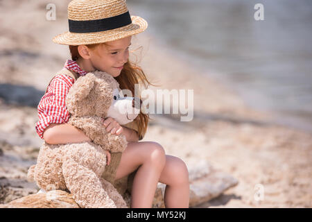 Nachdenkliche kleine Mädchen umarmt Teddybären und weg schauen beim Sitzen auf Meer Stockfoto