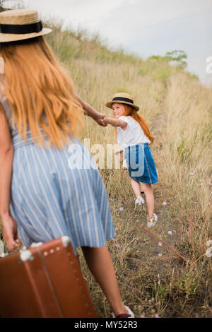 Mutter und Tochter mit Koffer und Teddybär, Hände beim Gehen auf Grünland Stockfoto