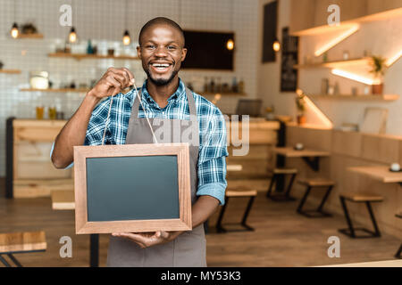 Lächelnd männlichen afrikanischen amerikanischen Inhaber der Coffee Shop Holding kleine leere Tafel in Holzrahmen Stockfoto