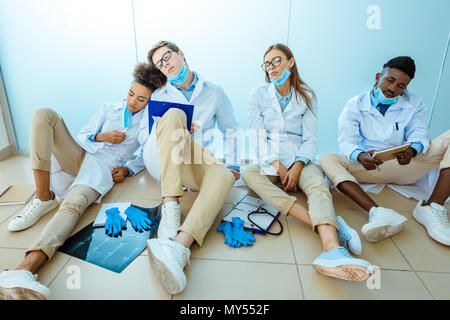 Gruppe medizinische Praktikanten sitzen auf dem Boden im Krankenhaus Flur erschöpft Napping Stockfoto