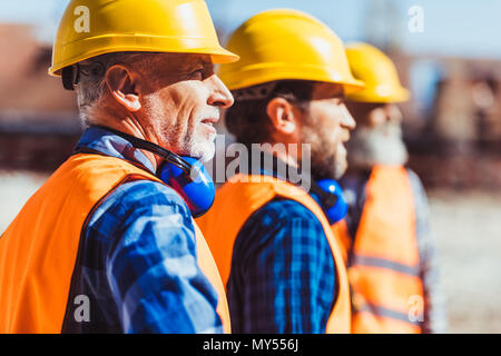Bauherren in Warnwesten und hardhats zusammen an der Baustelle stehen, auf der Suche nach Entfernung Stockfoto
