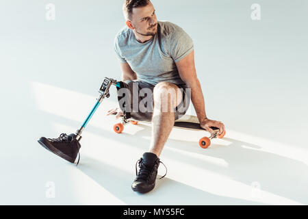 Junger Mann mit Bein Prothese sitzt auf Skateboard isoliert auf weißem Stockfoto