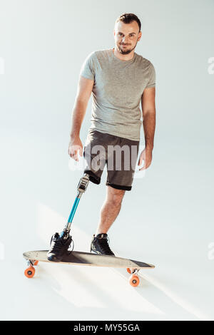 Lächelnder Mann mit beinprothese auf Skateboard und Kamera isoliert auf weißem Stockfoto