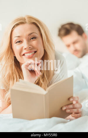 Junge Frau lesen Buch im Bett mit unscharfen auf Hintergrund Freund Stockfoto