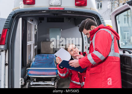 Gerne männliche und weibliche Sanitäter Lesen von Dokumenten vor der Ambulanz Stockfoto