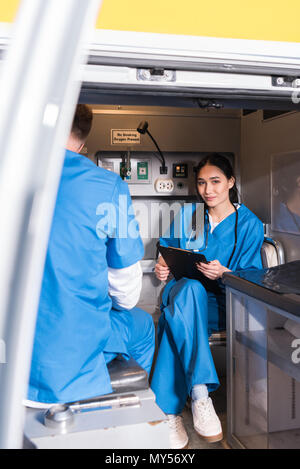 Lächelnd asiatischen Sanitäter holding Zwischenablage und Sitzen in der Ambulanz Stockfoto