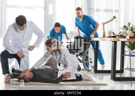 Junge ärzte Kontrolle Puls der unbewussten Mann liegen auf einer Etage im Krankenhaus Stockfoto