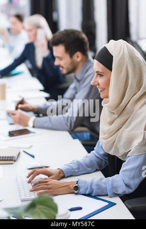Selektiver Fokus der lächelnden arabisch Geschäftsfrau im hijab Eingabe über Tastatur am Arbeitsplatz im Büro Stockfoto