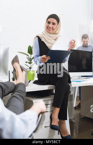Selektiver Fokus der lächelnden arabisch Geschäftsfrau im hijab mit Notizblock in der Hand sitzen am Tisch im Büro Stockfoto