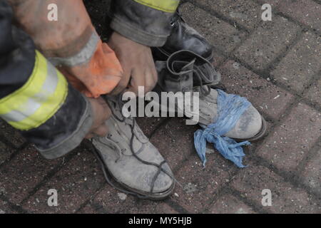 San Juan Alotenango, Guatemala. 05 Juni 2018, Guatemala, San Juan Alotenango: Mitglied der Feuerwehr Krawatten seine Schuhe bei den Rettungsarbeiten nach dem Vulkanausbruch des Volcan De Fuego (Feuer Vulkan). Nach der Eruption, rescue Teams waren mit schrecklichen Anblick konfrontiert. In einigen Häusern, die von den Klippen der Vulkan, entdeckten sie ganze Familien, die in der Katastrophe gestorben. Mindestens 70 Menschen wurden bei dem Vulkanausbruch ums Leben. Foto: Alejandro Balan/dpa Quelle: dpa Picture alliance/Alamy leben Nachrichten Stockfoto