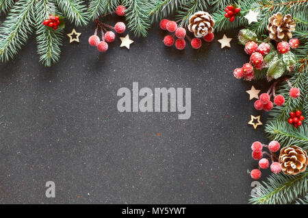 Weihnachten Hintergrund: Grenze mit fir Zweige, Beeren dekoriert und Frosted Tannenzapfen auf dunklen grunge Hintergrund, Text Raum Stockfoto