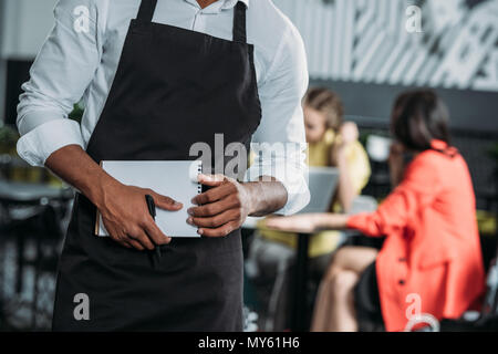 7/8 Schuß von Kellner Schürze mit Notepad im Cafe Stockfoto