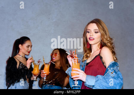 Schönen lächelnden Jungen stilvolle Frau mit Glas mit Cocktail, während multiethnischen Freunde hinter stehend Stockfoto