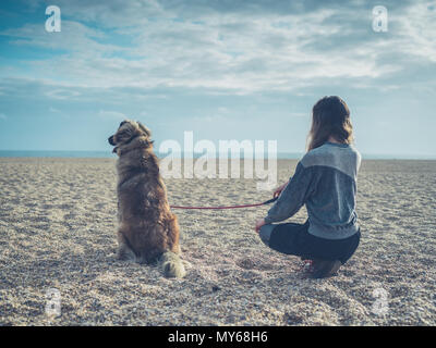 Eine junge Frau sitzt am Strand mit ihren großen Leonberger Hund Stockfoto