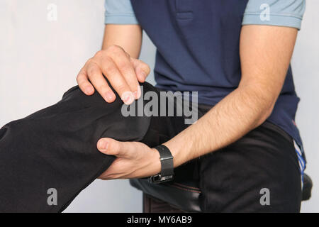 Athleten leiden unter Knieschmerzen. junger Mann hält seine Hände über seinen kranken knie auf einem blauen Hintergrund. kniescheibe Fraktur. Stockfoto