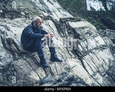 Ein älterer Mann sitzt auf ein paar Felsen am Meer Stockfoto