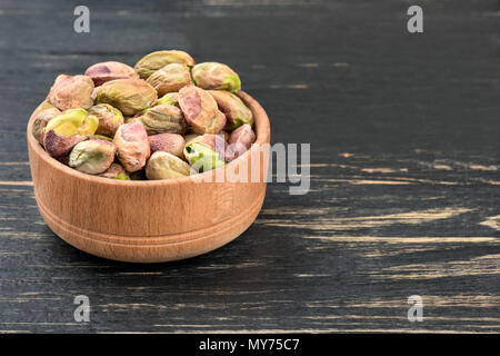 Pistazien ohne Schale in eine hölzerne Schüssel auf einen dunklen Tisch Stockfoto