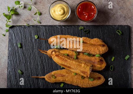 Vier frischen Mais Hunde o eine Dunkle Schiefer mit Tomatensauce und Senf - Ansicht von oben Stockfoto