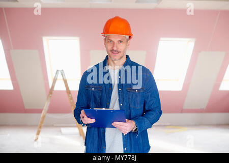Im mittleren Alter Heimwerker tragen, hardhat und Halten der Zwischenablage in der Hand beim Stehen an der Baustelle. Stockfoto