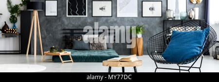 Black Diamond Stuhl mit blauem Kissen und offenes Buch am Ende Tabelle steht in dunklen Zimmer Interieur mit verschwommenen Hintergrund Stockfoto