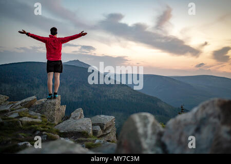 Mann feiern Sonnenuntergang am Berg. Auf inspirierende Aussicht. Trail Runner, Wanderer oder Bergsteiger erreicht Gipfel, geniessen Sie inspirierende Landschaft Stockfoto