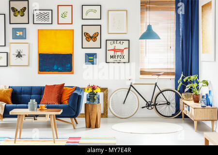 Echten Foto von einem retro Bike stehen neben dem Fenster im hellen Wohnzimmer Interieur mit navy blue settee, Holzschrank, orange Malerei und Post Stockfoto