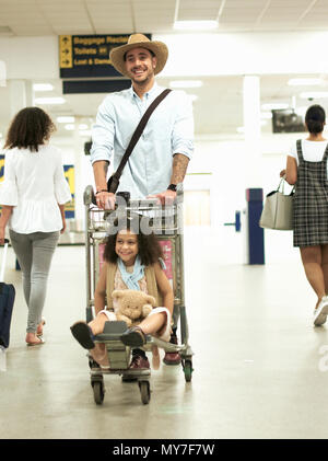 Vater mit Mädchen auf Gepäckwagen in Flughafen Stockfoto