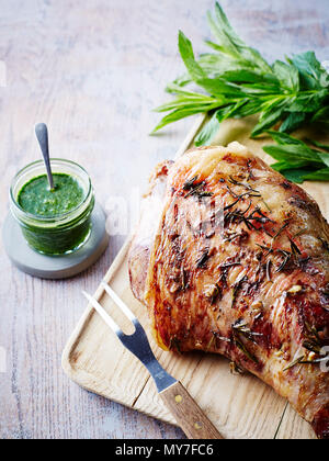 Gebratene Lammkeule auf Schneidebrett mit Glas mint Sauce, close-up Stockfoto