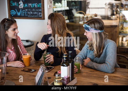 Drei junge weibliche Freunde mit Gemüsesaft im Cafe chatten Stockfoto