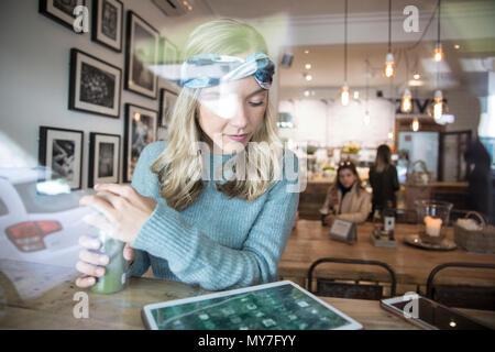 Junge Frau mit gemüsesaft am digitalen Tablette im Cafe Fensterplatz suchen