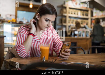 Junge Frau im Cafe sitzen, mit Smartphone, Smoothie am Tisch vor ihr