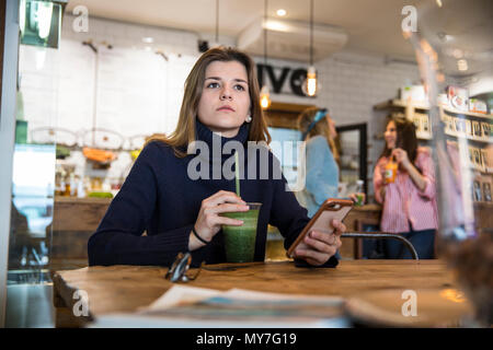 Junge Frau im Cafe sitzen, Smartphone, trink Smoothie Stockfoto