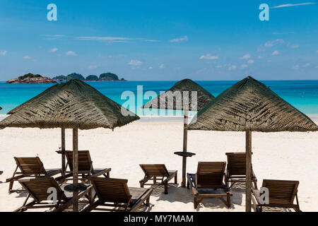 Typische Holiday Beach Landschaft mit hölzernen Sonnenliegen im Schatten der Sonnenschirme aus Holz mit Reetdach in der Mitte vom feinen weißen Sand. Stockfoto