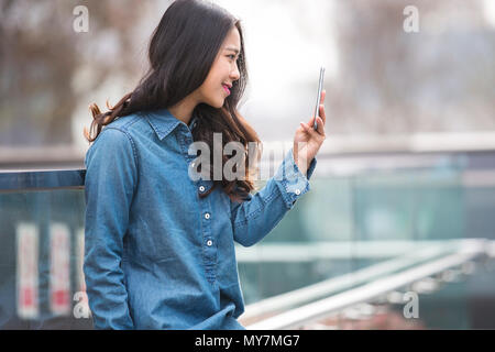 Foto von einem schönen jungen chinesischen Frau mit Handy outdoor im Straße Stockfoto